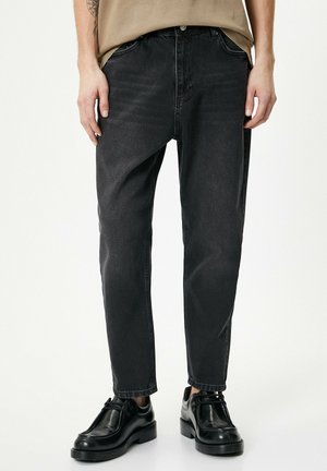 Pantaloni in denim neri con una vestibilità rilassata, dotati di chiusura a bottone, cinque tasche e leggere scoloriture per texture. Abbinati a calzature nere.