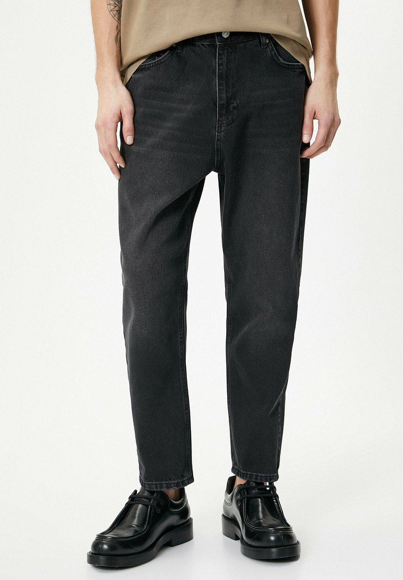 Pantalones de mezclilla negros con un corte relajado, que cuentan con un cierre de botón, cinco bolsillos y un ligero desgaste para dar textura. Combinados con calzado negro.
