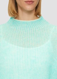 Pull en tricot côtelé bleu clair avec un col haut et une texture transparente. Le tissu semble doux et léger, idéal pour superposer.