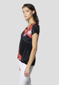 Melna īsroku T-krekls ar lielu sarkanu ziedu rakstu, apaļu kakla izgriezumu un brīva piegriezuma, kombinēts ar biksēm baltā krāsā. Mīksta auduma tekstūra.