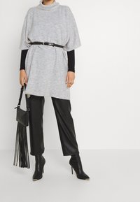 Šedá pletená oversized tunika s rolákem, stažená v pase černým opaskem, spárovaná s lesklými černými kalhotami z umělé kůže a botami na podpatku.