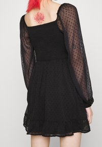 Black dress with a smocked bodice, sheer puff sleeves, and a ruffled hem. Features a dotted texture and a flared silhouette.