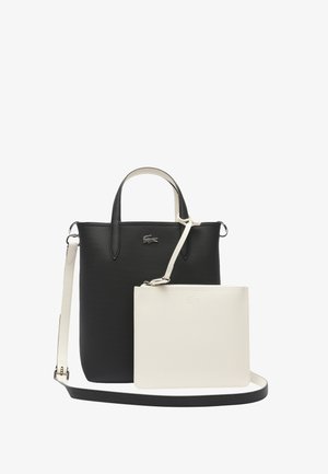 Sac fourre-tout synthétique noir texturé avec poignées doubles, une pochette en cuir blanc détachable et une bandoulière réglable. Détail du logo Lacoste.