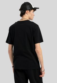 Czarna bawełniana koszulka z krótkim rękawem, okrągłym dekoltem i luźnym krojem. Model nosi czapkę czarno-białą oraz akcesoria.