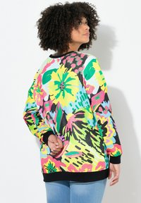 Sweatshirt à motif floral coloré dans des teintes vives de jaune, rose et vert. Il présente une coupe décontractée, des poignets larges et un col arrondi.