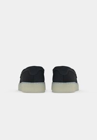 Sneaker basse in suede nero con una texture liscia, dotate di una suola in gomma chiara e un design minimalista.