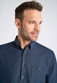 Camicia blu navy con bottoni, realizzata in un tessuto testurizzato, colletto e una singola taschino sul petto con bottoni argentati. Design semplice e strutturato.