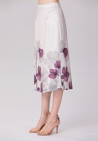 Jupe midi blanche avec des motifs floraux violets sur l'ourlet, fabriquée en tissu doux. Fermeture éclair au dos.