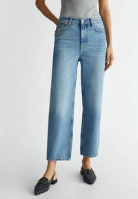 Ljusblå, högmidjade jeans med rak bendesign, subtila blekningar, femficksstil och metallknappsstängning. I kombination med svarta slingbacks.