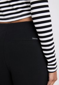 Svarta byxor med en elegant design, med en bakficka och en Calvin Klein-logotyp. Den randiga långärmade toppen har vita och svarta horisontella ränder.