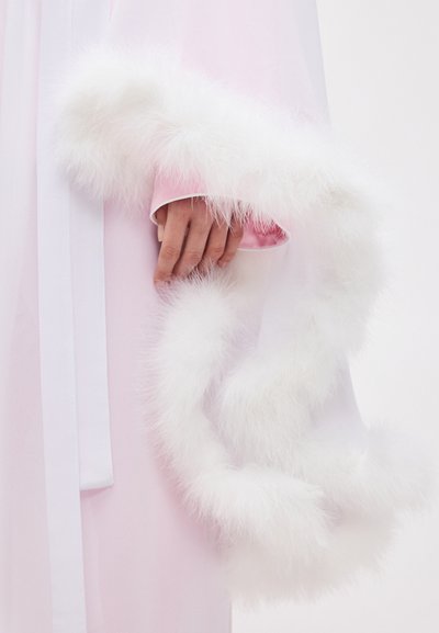 Χέρι με ροζ σατέν μανίκι που κρατά λευκή, αφράτη μποά φτερών, με φόντο ροζ ρούχο.