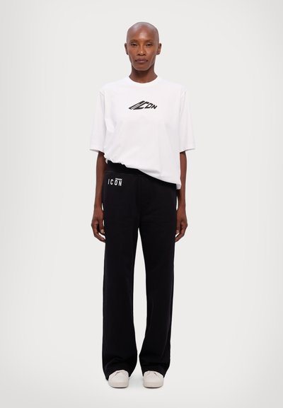 Weißes Baumwoll-T-Shirt mit schwarzem Logo, kombiniert mit schwarzen Jogginghosen, die ein weißes Seitenlogo tragen, beide in lockerer Passform mit glatter Textur.