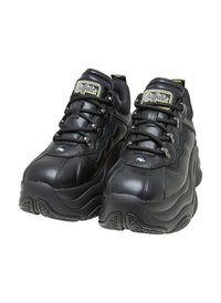 Schwarze Sneaker mit einem glatten Lederobermaterial, Mesh-Akzenten, dickem Gummisohle und kontrastierendem gelbem Logo auf der Zunge.