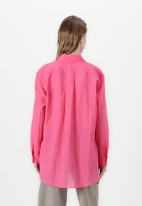 Langärmliges Shirt in leuchtendem Pink, aus leichtem Stoff gefertigt. Verfügt über einen klassischen Kragen, eine leicht strukturierte Oberfläche und einen abgerundeten Saum.