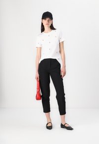 Witte t-shirt met kleine rode kersenprints, zwarte op maat gemaakte broek, zwarte pet, rode handtas en zwarte studschoenen. Minimalistisch ontwerp, casual uitstraling.