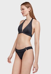 Crni bikin set koji sadrži halter-top s dubokim V-izrezom i trokutastim čašicama, s podesivim vezicama, uparen s donjim dijelom s niskim strukom i bočnim izrezima.