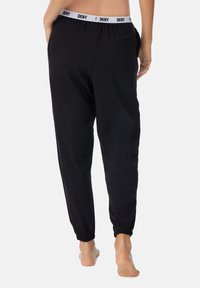 Zwarte joggingbroek van zacht materiaal, met een elastische tailleband voorzien van het "DKNY"-logo en elastische boorden bij de enkels.