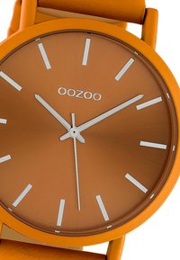 Orange silicone watch with a matte finish, featuring a round dial, white indices, and the brand name "OOZOO" centered on a brown background.