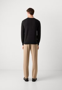 Pull en tricot noir avec un col rond, des manches longues et une coupe droite, associé à un pantalon beige ajusté, vu de dos.
