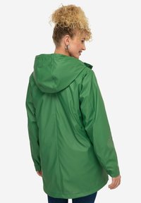 Giacca impermeabile verde con cappuccio, caratterizzata da una texture morbida e un fit rilassato. La vista posteriore mostra un taglio dritto e senza chiusure visibili.