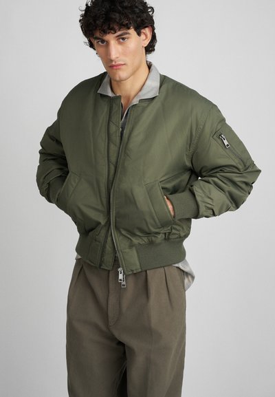 Chaqueta bomber verde oliva con cierre frontal, puños y dobladillo acanalados, que presenta bolsillos laterales y un cuello gris en contraste.
