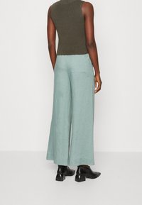 Zielony dzianinowy top bez rękawów w połączeniu z luźnymi, jasnoniebieskimi lnianymi spodniami o szerokich nogawkach. Czarne botki za kostkę dopełniają całość.