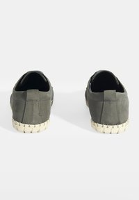 Baskets slip-on en toile verte avec une finition texturée, présentant une semelle tissée contrastante. La vue arrière met en avant le design épuré de la chaussure.