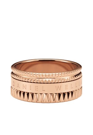 Bague en or rose avec des bandes texturées et lisses, gravée DANIEL WELLINGTON, avec des détails géométriques en forme de pyramide.