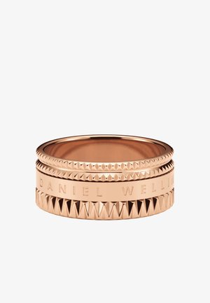 Bague en or rose avec des bandes texturées et lisses, gravée DANIEL WELLINGTON, avec des détails géométriques en forme de pyramide.
