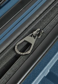 Valigia rigida blu con tessuto nero testurizzato, una cerniera argentata con un'etichetta espandibile e linee di accento blu in contrasto.