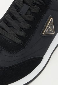 Sorte sneakers laget av semsket skinn og mesh-materiale, med teksturerte lisser, slank design, hvit mellomsåle og et trekantet gullmerke.