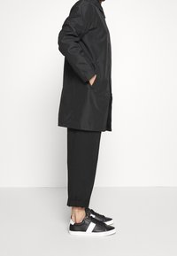 Black lightweight coat with a straight cut, two side pockets. Matched with tapered black pants and black sneakers featuring white accents.
