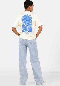 Cremefarvet t-shirt med korte ærmer, prydet med blå palmetræ grafik, sat sammen med lyseblå vidde jeans. Simpelt design, afslappet pasform, ingen synlige mønstre.