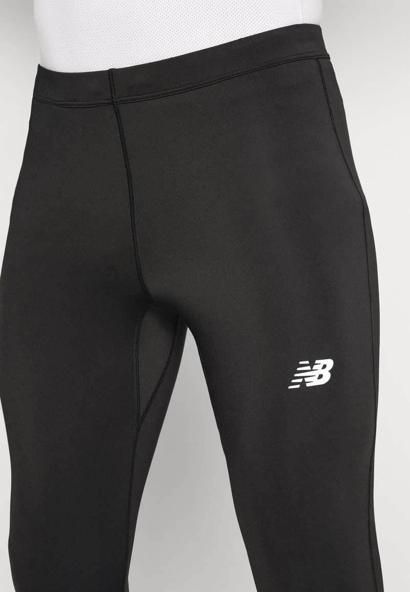 Schwarze Sportleggings aus dehnbarem Material mit Flachnaht und einem weißen "NB"-Logo am Unterschenkel.
