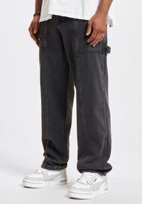 Pantalones cargo gris oscuro con costuras visibles, bolsillos laterales y un corte holgado, combinados con zapatillas blancas y grises.