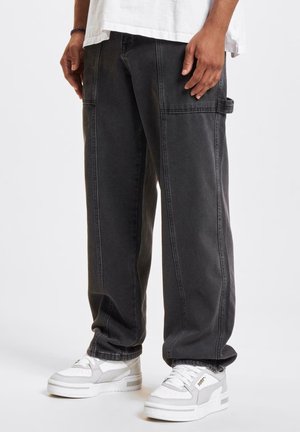 Pantalones cargo gris oscuro con costuras visibles, bolsillos laterales y un corte holgado, combinados con zapatillas blancas y grises.