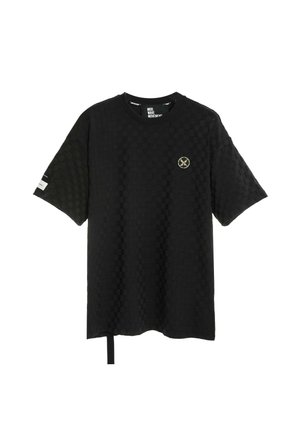 Camiseta negra de manga corta con textura, con pequeño emblema redondo en el pecho izquierdo y detalle de etiqueta blanca en la manga derecha.
