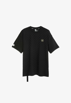 Camiseta negra de manga corta con textura, con pequeño emblema redondo en el pecho izquierdo y detalle de etiqueta blanca en la manga derecha.