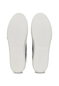Zapatos tipo slip-on de Tommy Hilfiger, con parte superior de tejido azul marino y suelas de goma blanca, presentan una textura en la suela y el logo de la marca en la parte inferior.