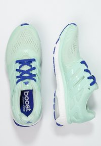 Jasnozielone buty do biegania z siateczkową cholewką, niebieskimi sznurowadłami i białą, amortyzowaną podeszwą. Z logo Adidas i teksturowanymi akcentami.