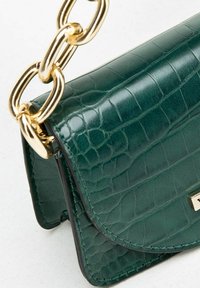 Sac à main en simili-cuir crocodile vert foncé avec fermeture à rabat et anse en chaîne dorée épaisse sur un fond clair.