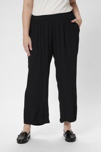 Schwarze, leichte, gefaltete Hose mit elastischem Bund und zwei seitlichen Taschen, kombiniert mit glänzenden schwarzen Slippern.