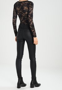 Body en dentelle noire à manches longues avec motif floral, associé à un pantalon en faux cuir noir brillant ajusté et des bottines.