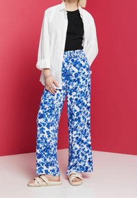 Blommiga vida byxor med en vit botten och blå blommönster, elastisk midja, kombinerat med en svart topp och en vit skjorta med knappar.