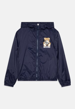 Navy windbreaker jacket with a hood, featuring a teddy bear graphic and the brand name "MUSCHINO" in white. Smooth, lightweight fabric.