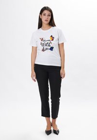 Hvid bomulds t-shirt med et farverigt sommerfugl-design og teksten "Altid med kærlighed." Sammen med sorte slim-fit bukser og sorte hæle.