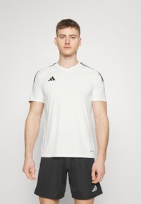 Camiseta atlética de manga corta blanca con franjas laterales negras. Presenta un cuello en V y el logo de Adidas en el lado izquierdo del pecho. Hecha de material transpirable.