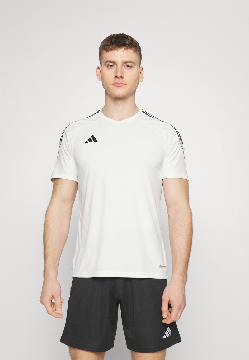 Camiseta atlética de manga corta blanca con franjas laterales negras. Presenta un cuello en V y el logo de Adidas en el lado izquierdo del pecho. Hecha de material transpirable.