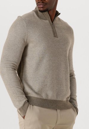 Hellbraunes, strukturiertes Strickpullover mit einem halben Reißverschluss-Kragen, ausgestattet mit einer taillierten Passform und geripptem Saum, getragen über beigen Hosen.