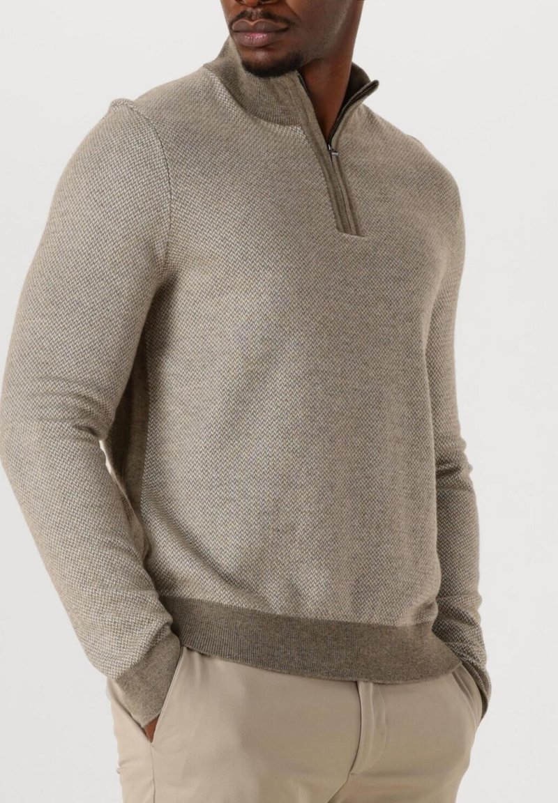 Hellbraunes, strukturiertes Strickpullover mit einem halben Reißverschluss-Kragen, ausgestattet mit einer taillierten Passform und geripptem Saum, getragen über beigen Hosen.